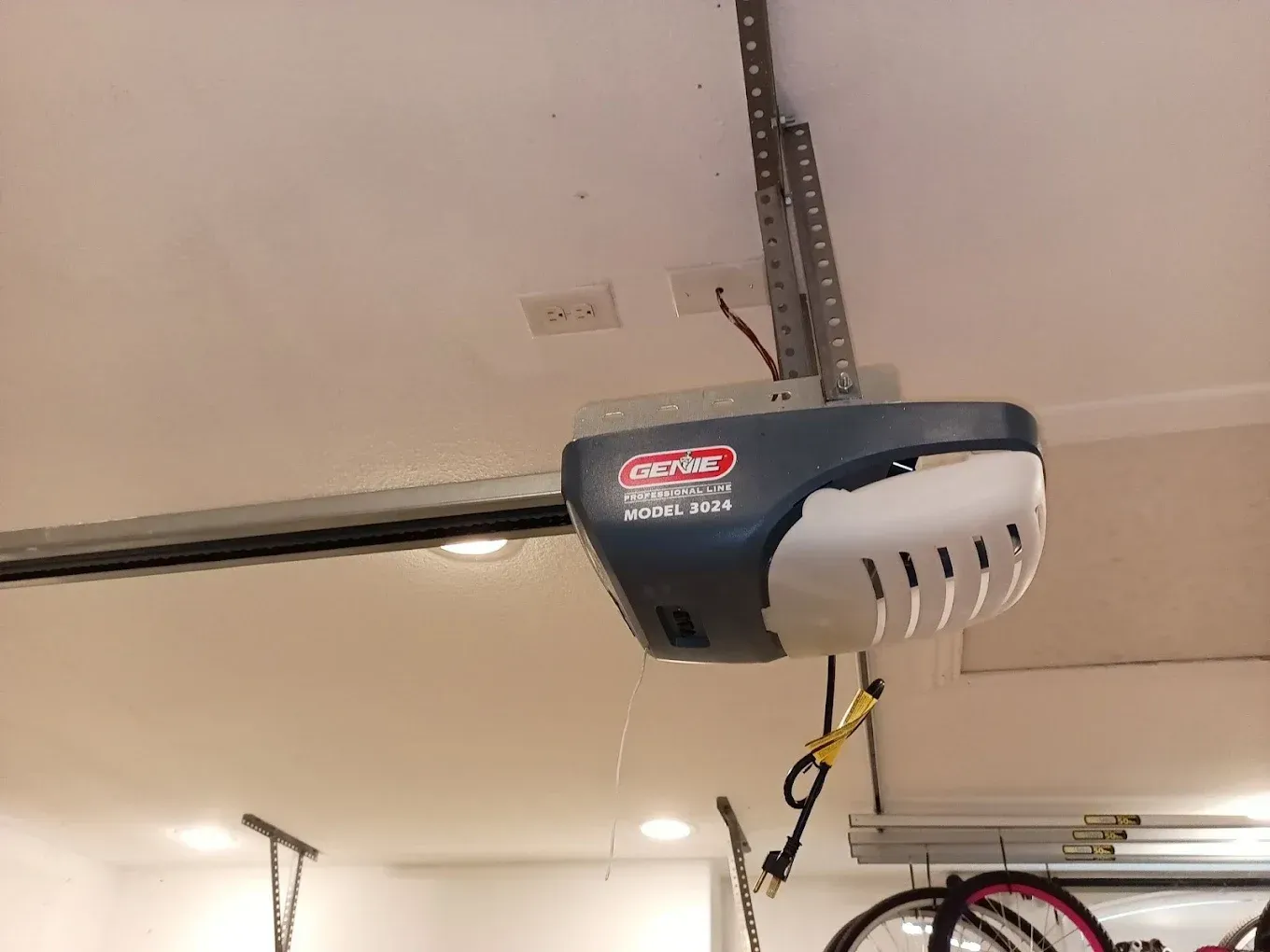 A Genie garage door opener mounted to a white ceiling in a garage.