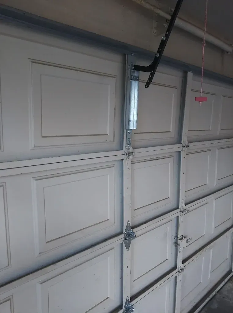 A close-up view of the interior of a white metal garage door, showing the vertical panels, hinges, and steel track.