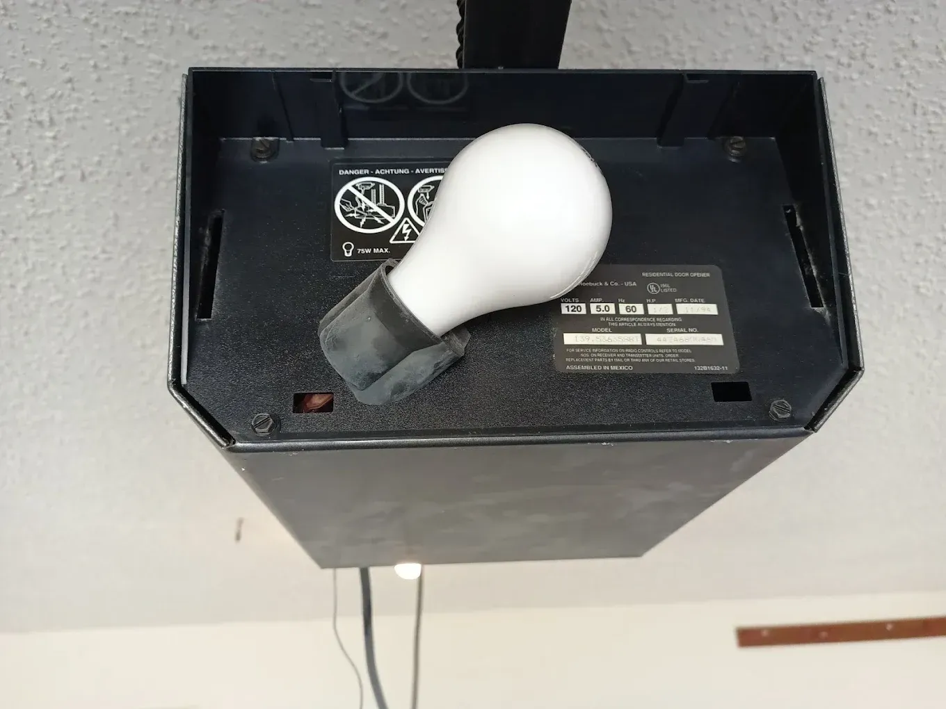 A garage door opener motor hanging from a ceiling, featuring an exposed light bulb in its housing.