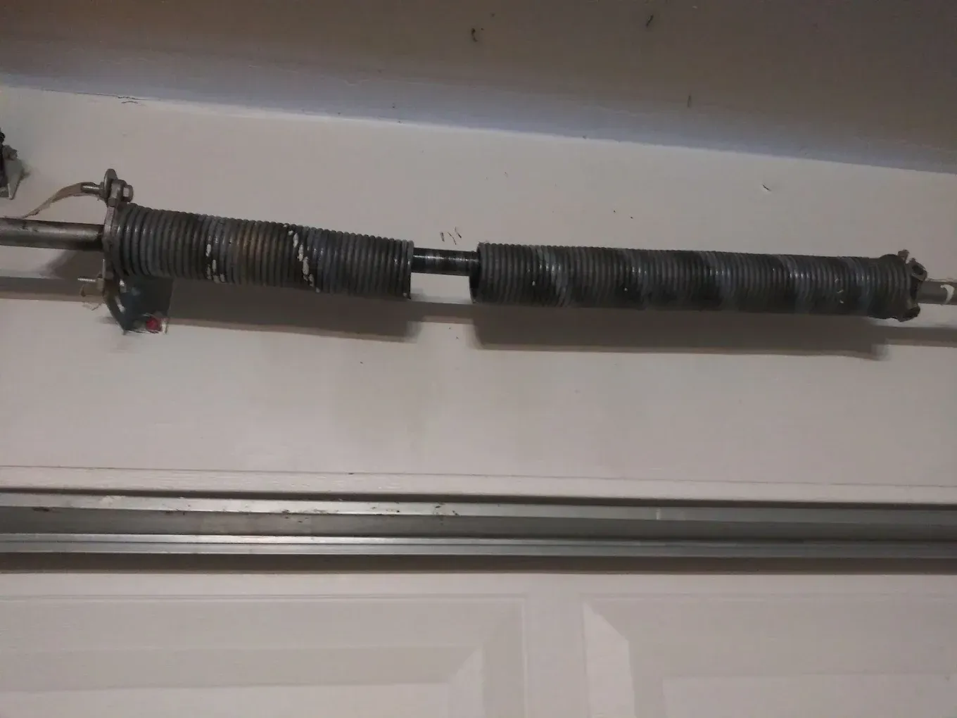 A broken garage door torsion spring, split into two pieces, mounted on a metal shaft above a door frame.