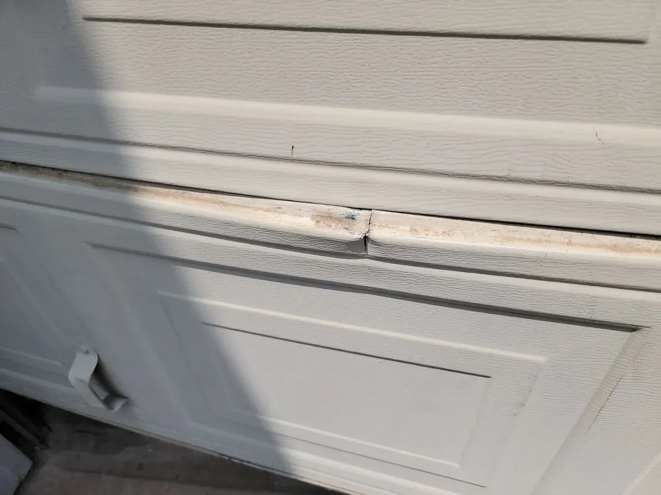 Close-up of a crack in the metal panel of a white residential garage door.