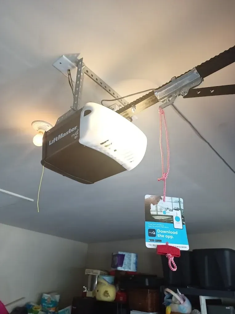 A LiftMaster garage door opener mounted to a ceiling with a red emergency release handle hanging below.
