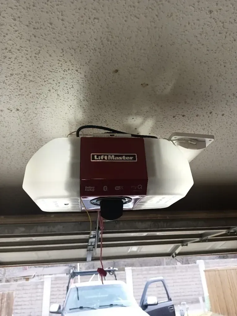 A white and maroon LiftMaster garage door opener mounted to a textured ceiling inside a garage.