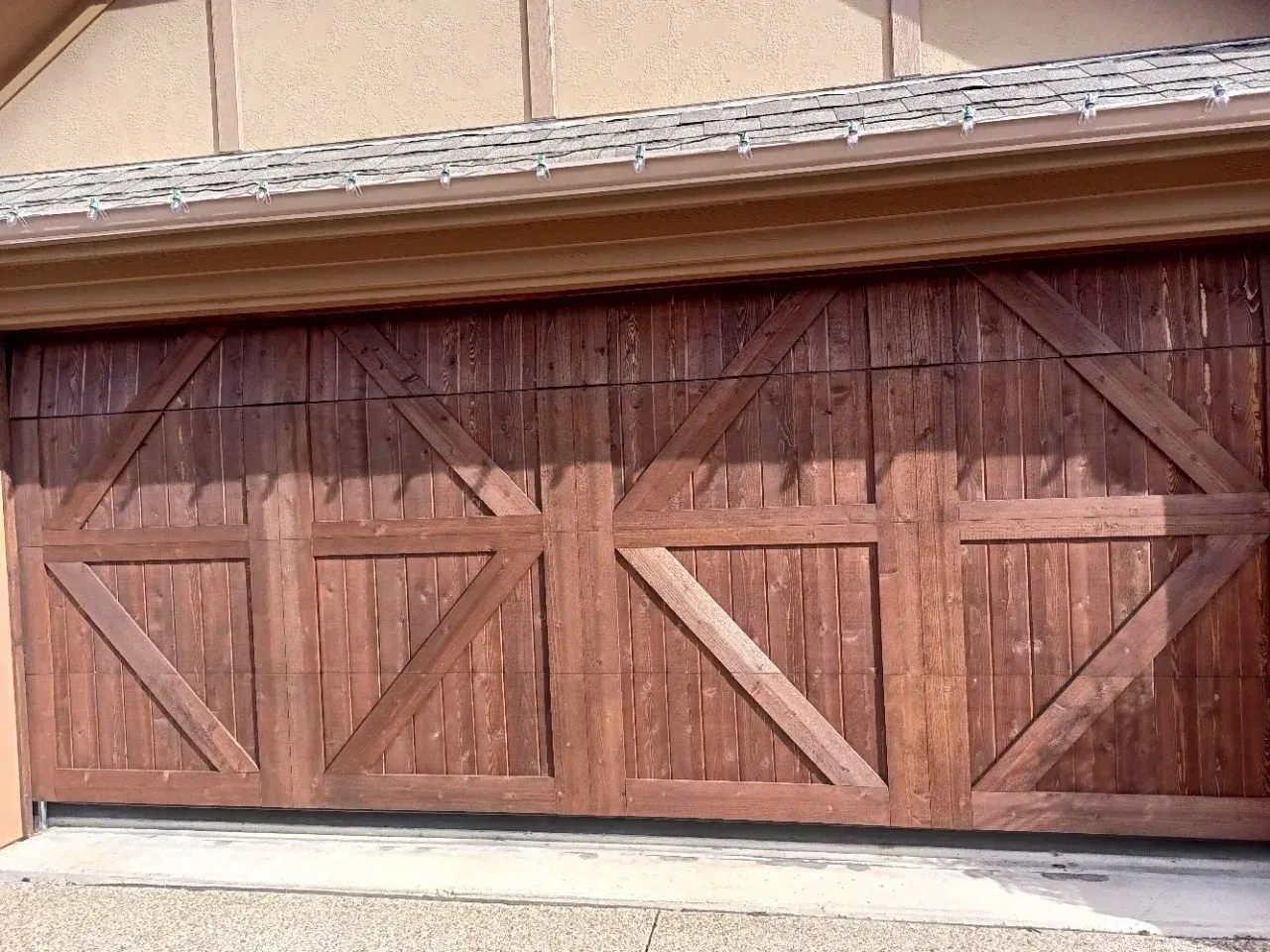 A wide, dark brown wooden garage door featuring a decorative, symmetrical X-frame pattern design.