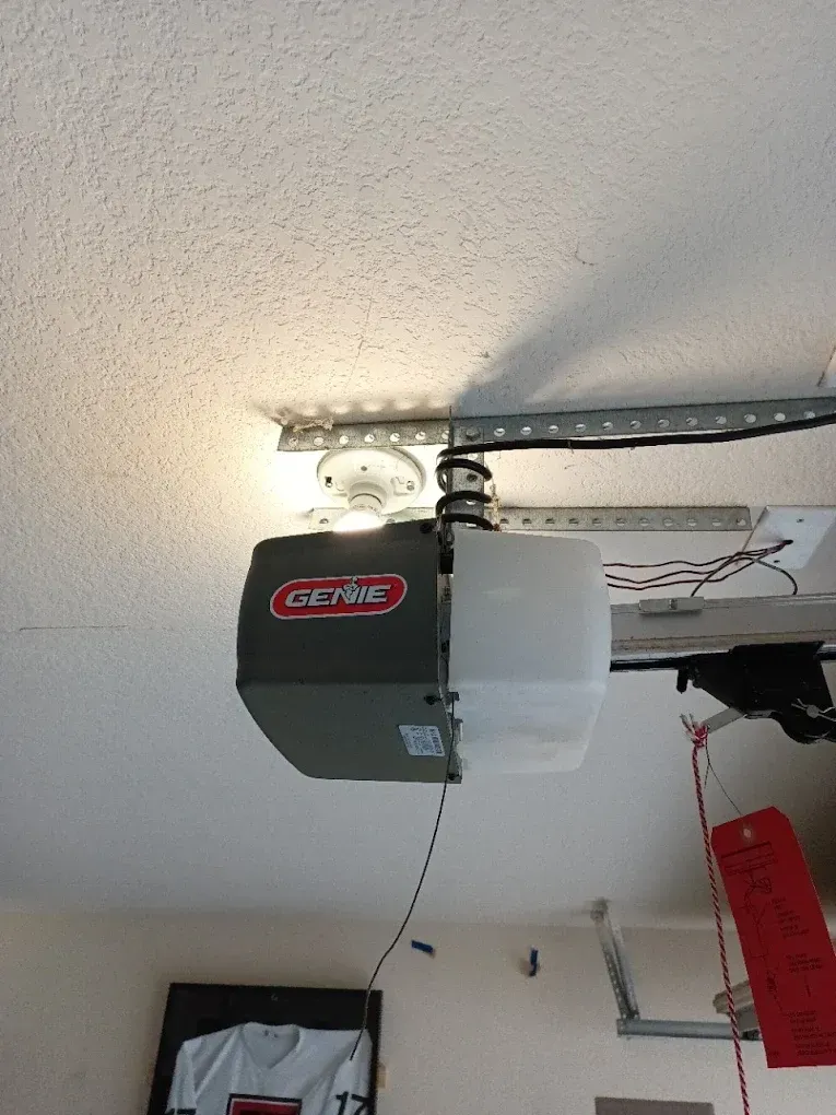 A Genie garage door opener mounted to a ceiling with its light turned on.