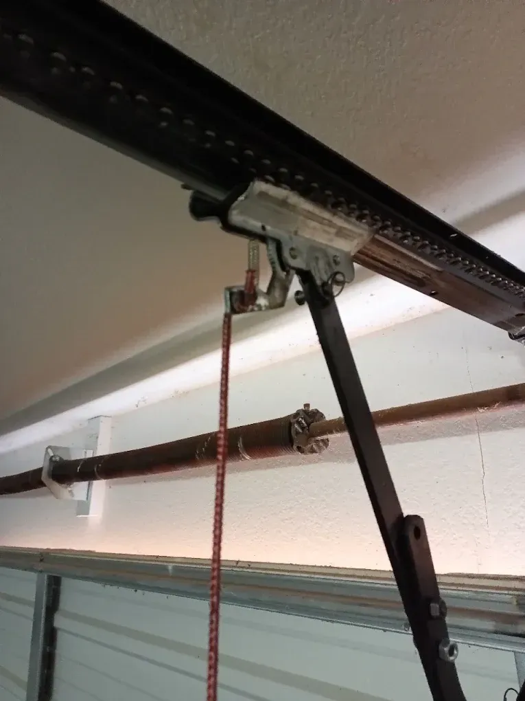 A garage door opener carriage and trolley mechanism mounted to a rail, with an emergency release cord hanging down.