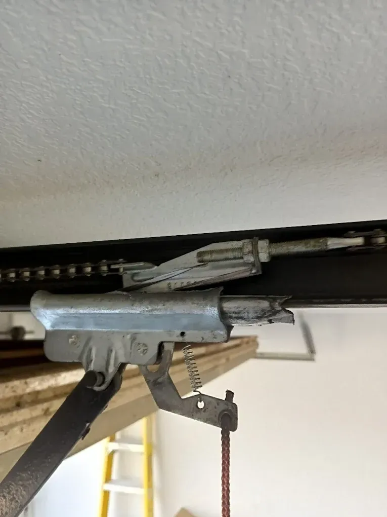A metal garage door opener trolley attached to a drive chain, with a red emergency release cord hanging below.