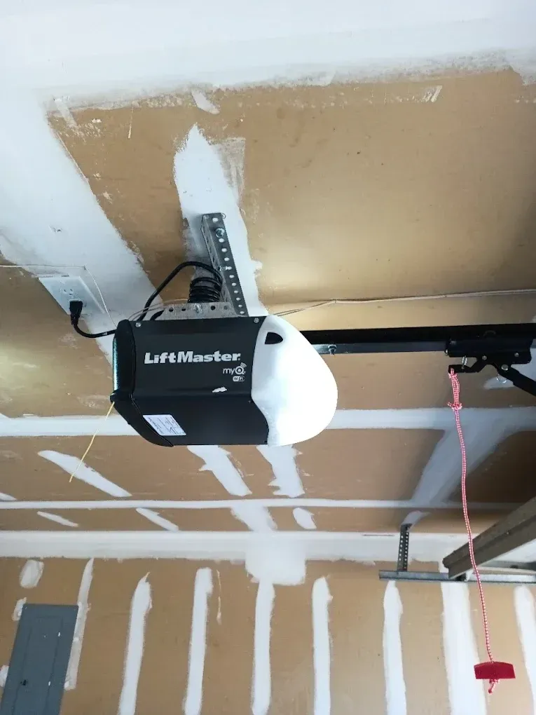 A black and white LiftMaster garage door opener mounted to a ceiling with exposed drywall.