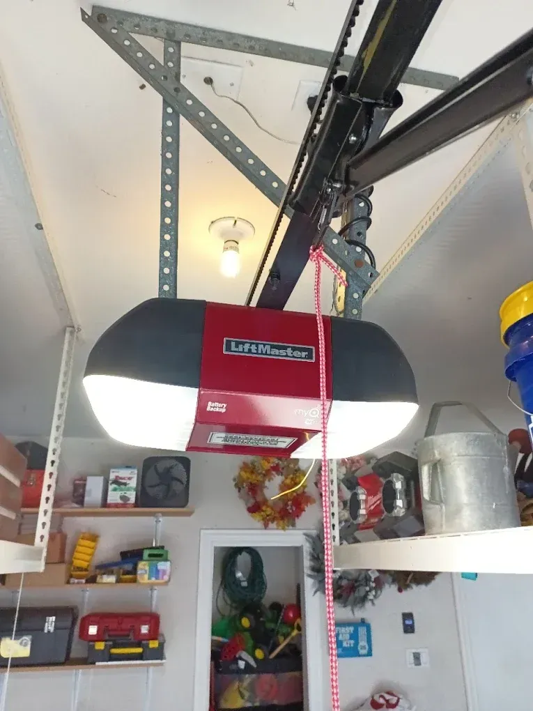 A red and black LiftMaster garage door opener mounted to a ceiling with a hanging red emergency release cord.