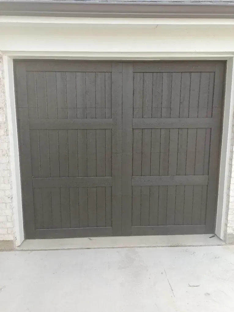 A dark brown wooden garage door with vertical slats and three horizontal panel sections, framed by a white brick exterior.