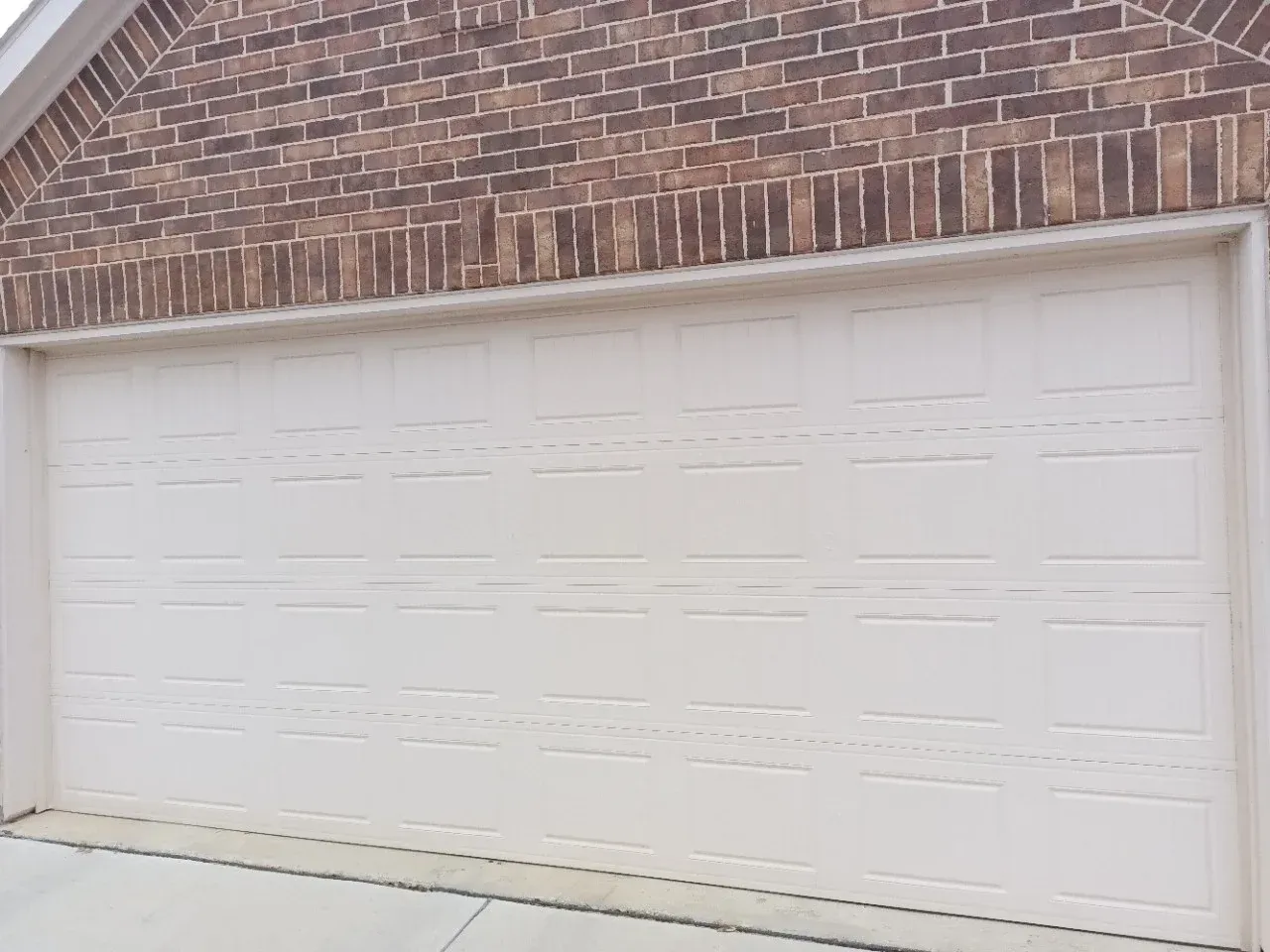 A white, multi-panel garage door set into a brick exterior wall.