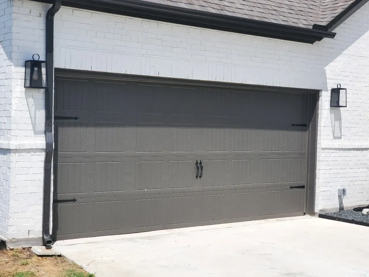 A modern dark grey garage door with decorative hinges and handles, installed in a white brick wall exterior.