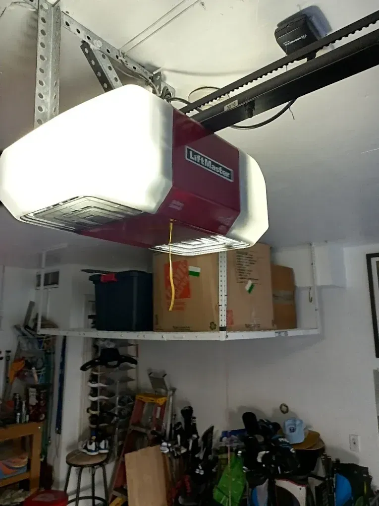 A red and white LiftMaster garage door opener mounted to the ceiling above storage boxes and various garage items.