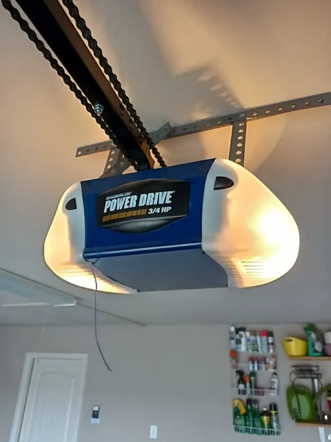 A white and blue Power Drive garage door opener with a chain-drive rail, mounted to a residential ceiling.