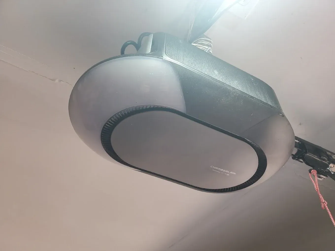 A modern gray garage door opener mounted to a ceiling with an integrated light cover.