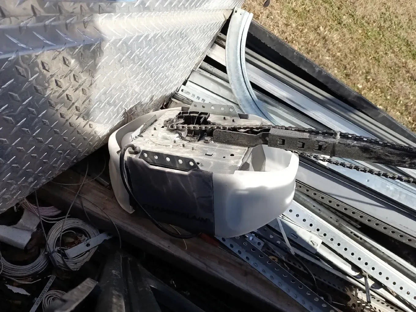 A chain-drive garage door opener unit sitting on a pile of metal scrap and construction materials.