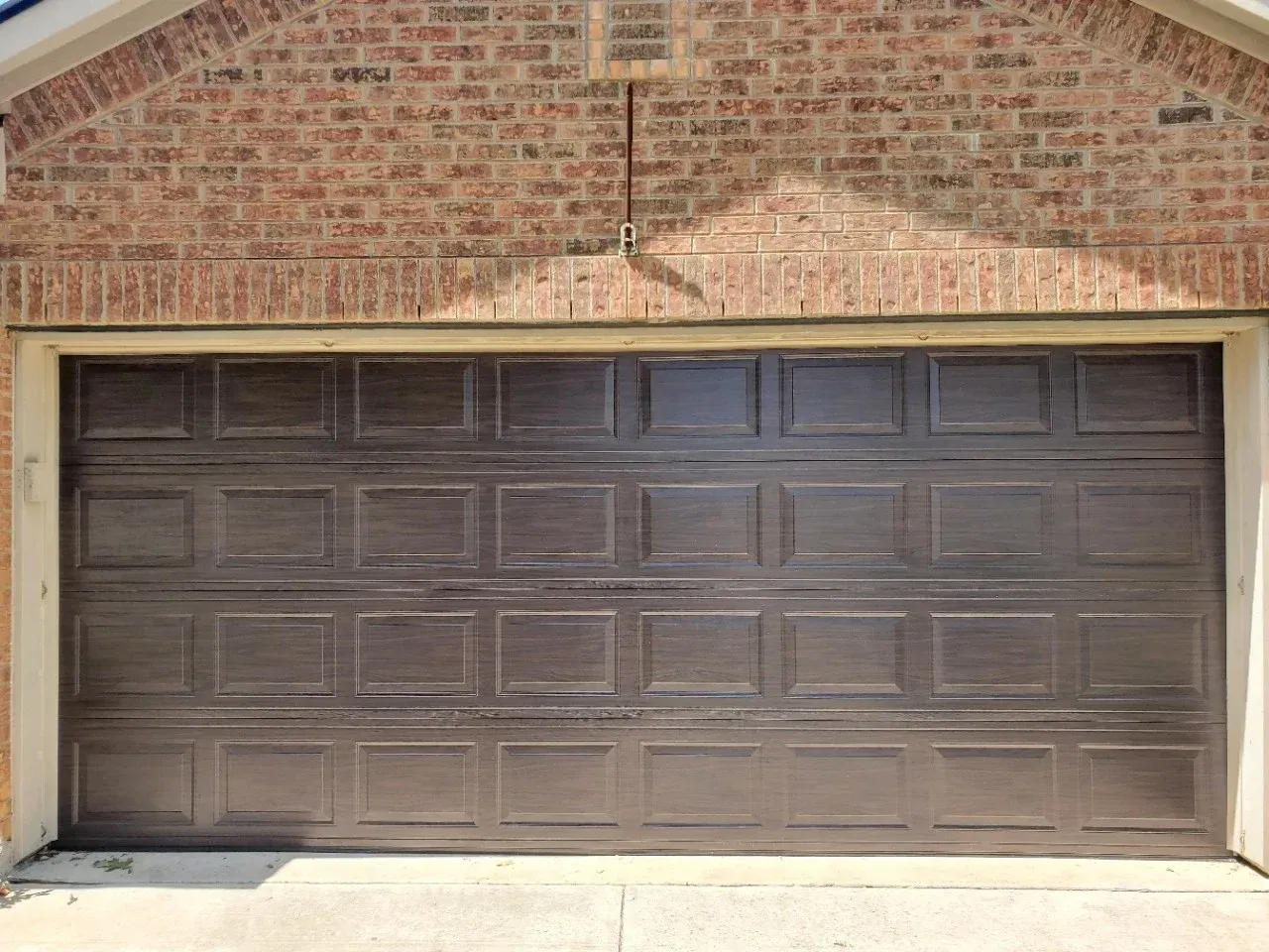 A dark brown, raised-panel garage door installed in a residential brick exterior wall.