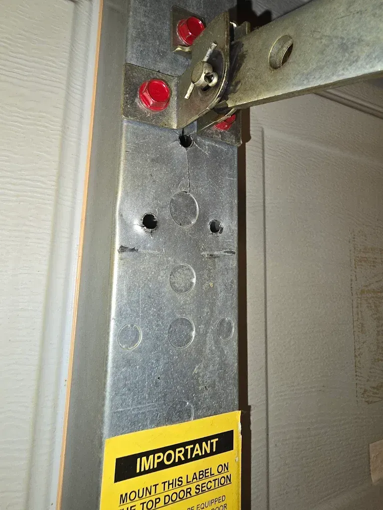 Close-up of a garage door bracket attached with red bolts, showing a vertical metal reinforcement strut on a white door.