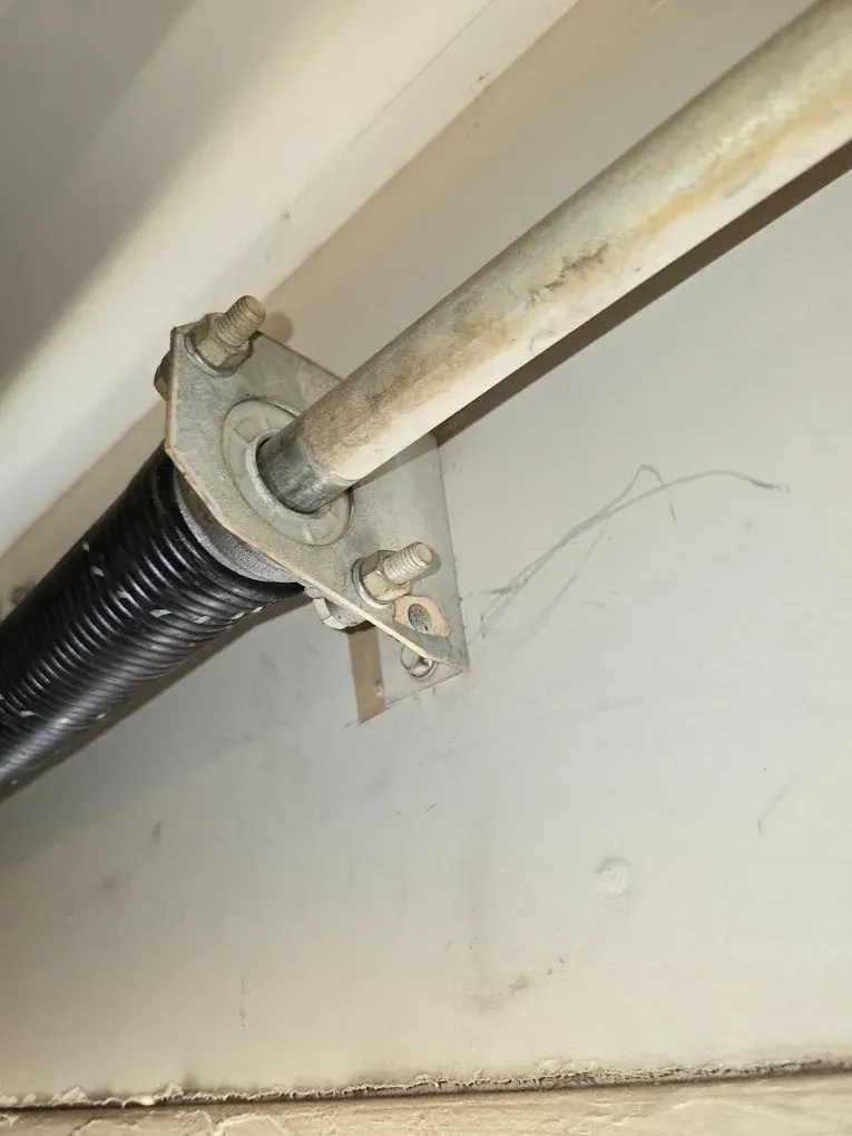 Close-up of a garage door torsion spring and metal bracket mounted to a wall.