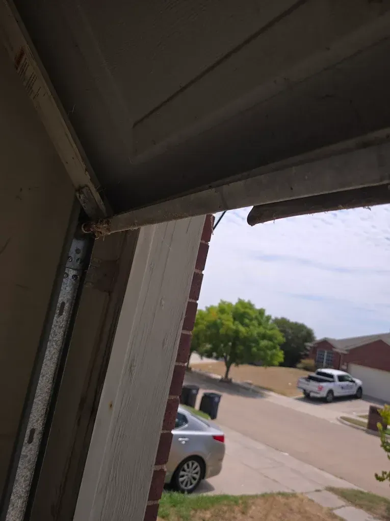 An angled view showing a damaged metal hinge or bracket hanging from the top edge of an open garage door.