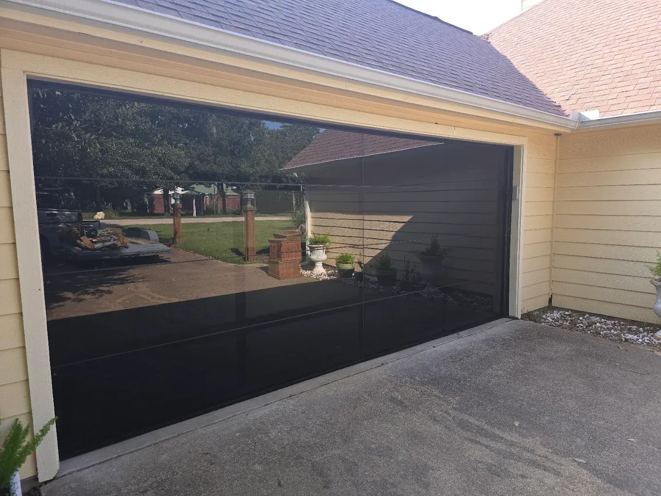 A modern black, reflective full-view garage door installed on a house with light yellow siding.