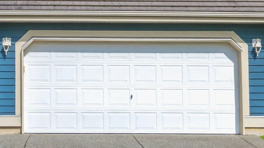 A closed white sectional garage door framed in light beige, set against blue horizontal siding on a house exterior.