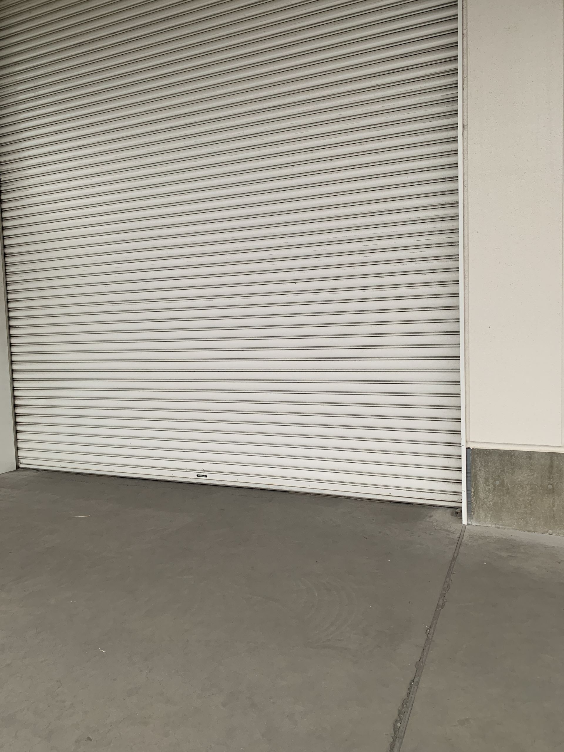 A white garage door featuring a black, wavy moiré pattern, set above a grey concrete floor next to a white wall.
