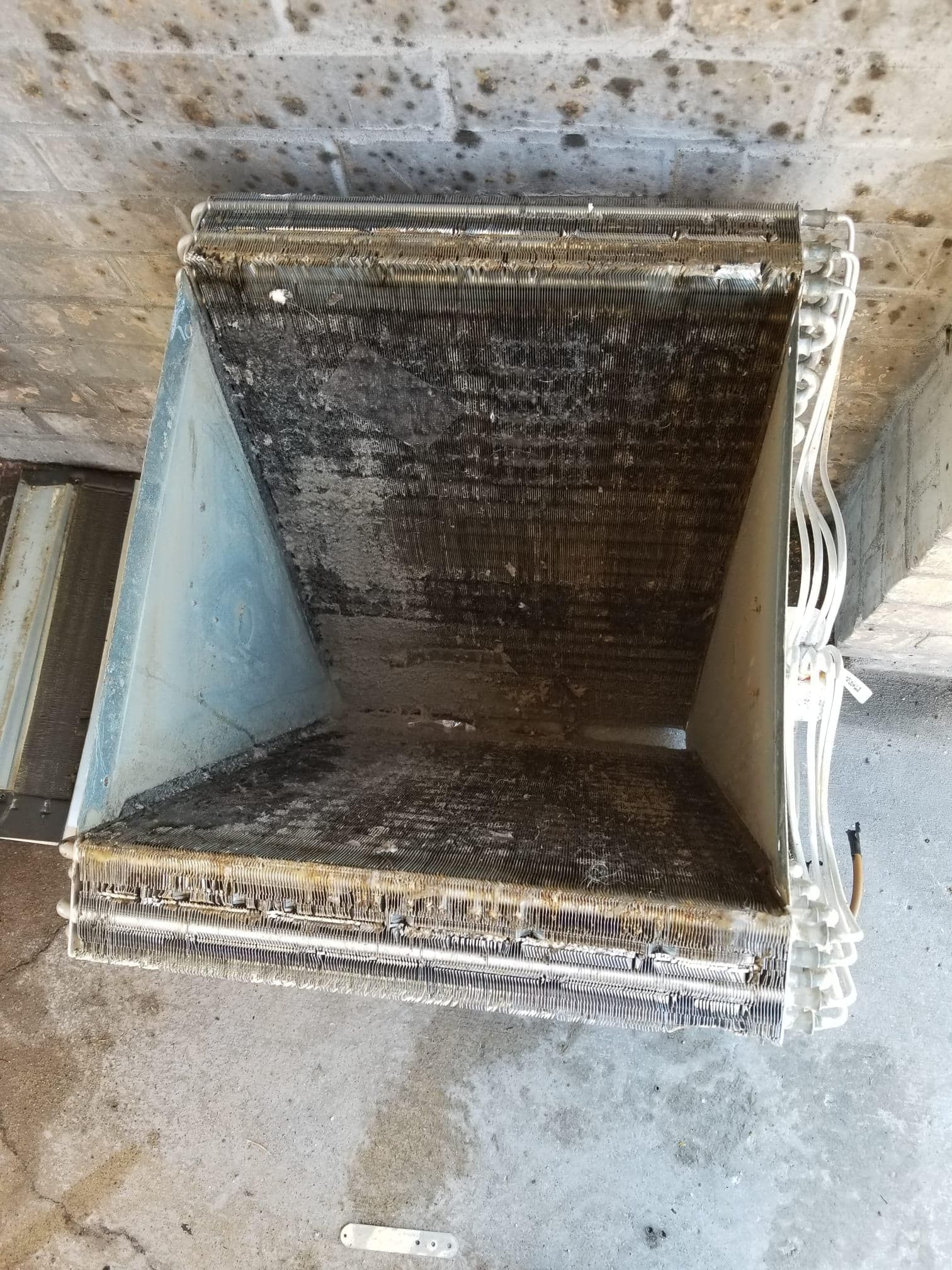 A dirty radiator is sitting on the ground next to a brick wall.