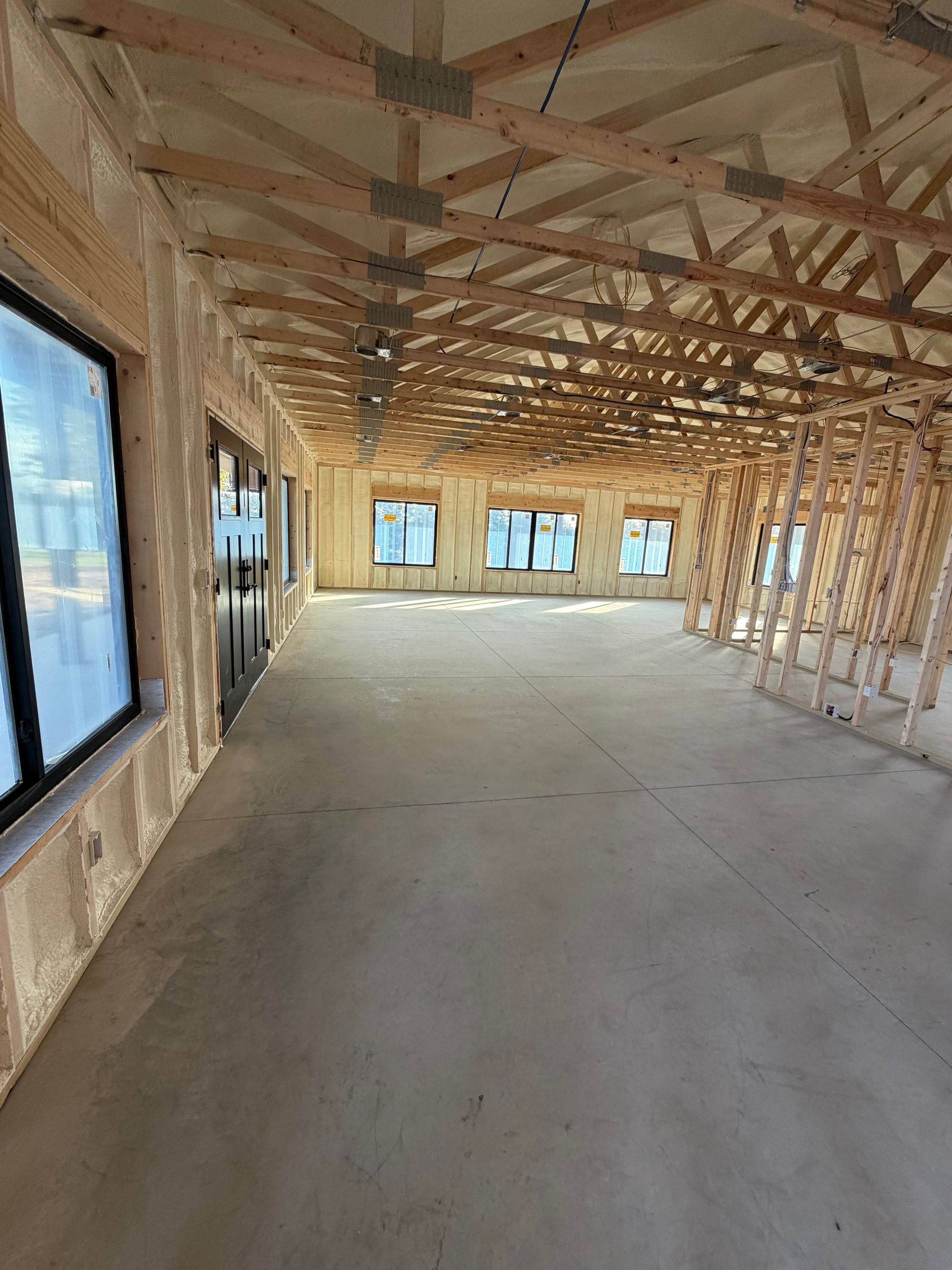 Unfinished house interior with exposed wooden framing, concrete floor, and large window openings.