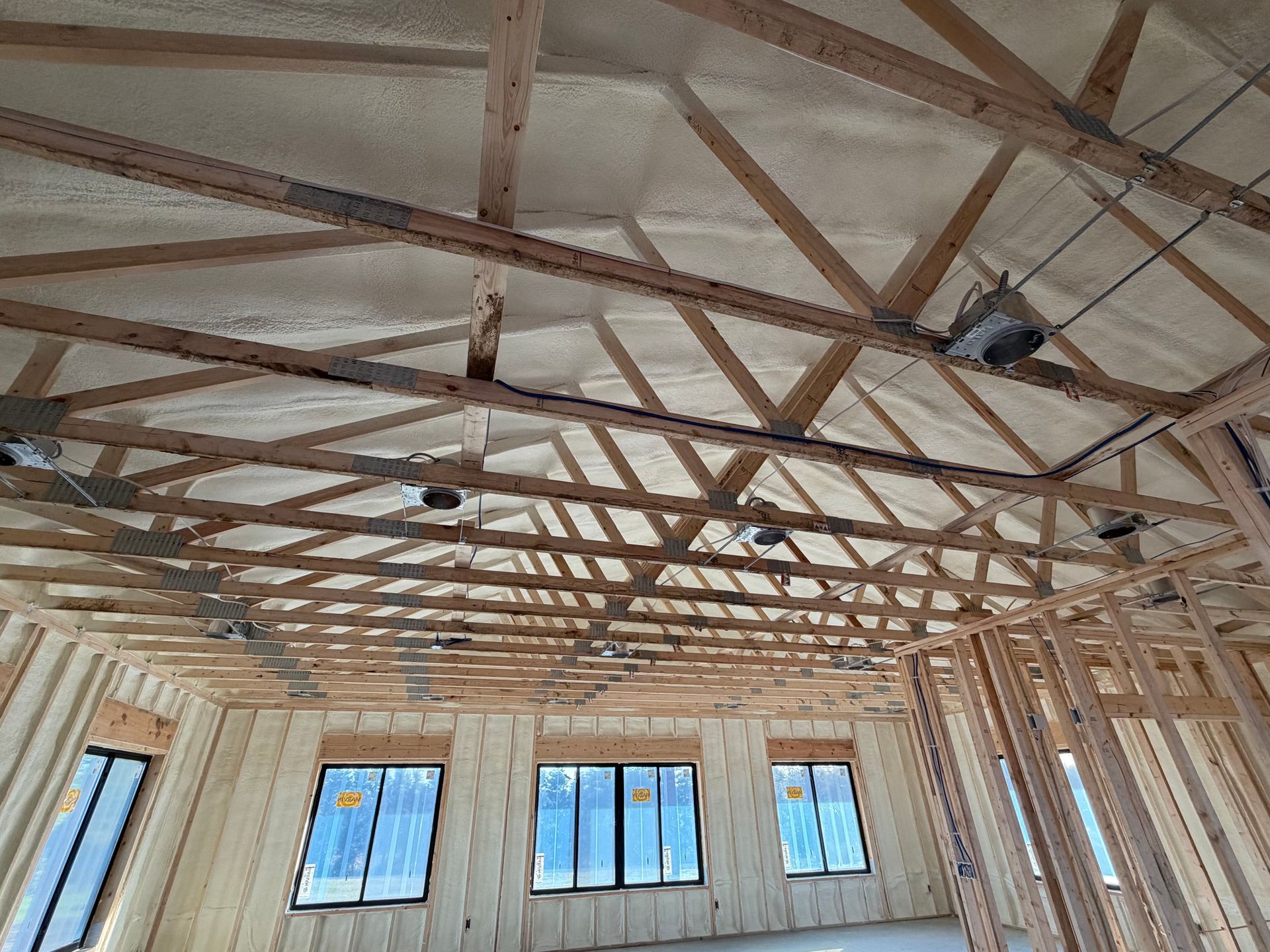 Interior of a wooden-framed building under construction, with exposed rafters and window openings.