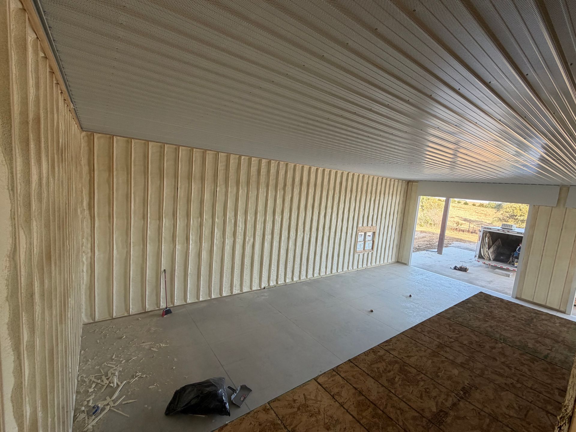 Empty room with wood-paneled walls, corrugated ceiling, and a concrete floor near an open doorway.