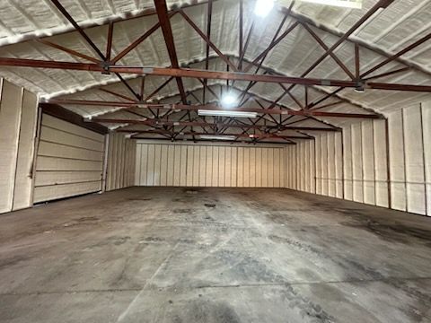Empty warehouse interior with concrete floor, white walls, and exposed red steel roof trusses