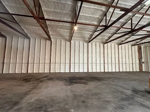 Empty industrial warehouse interior with white metal walls, exposed roof beams, and concrete floor
