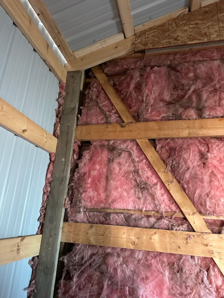 Interior wall with pink insulation, exposed wood framing, and a corrugated metal roof.