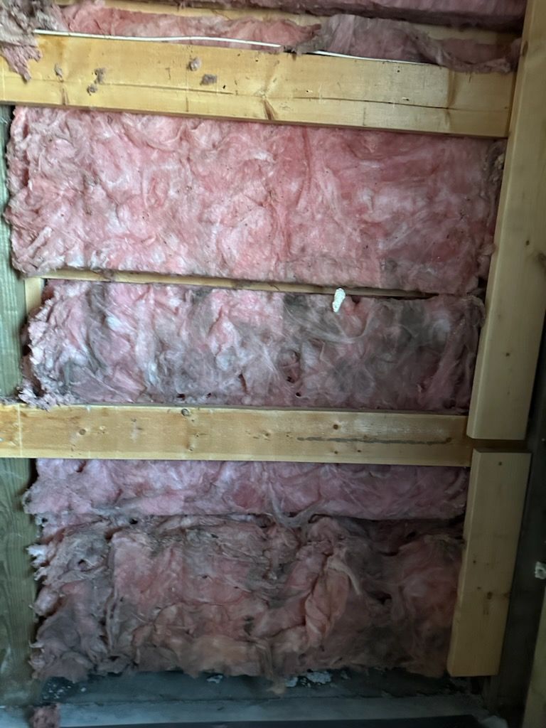 Pink insulation batts between horizontal wooden wall studs in an unfinished interior wall.