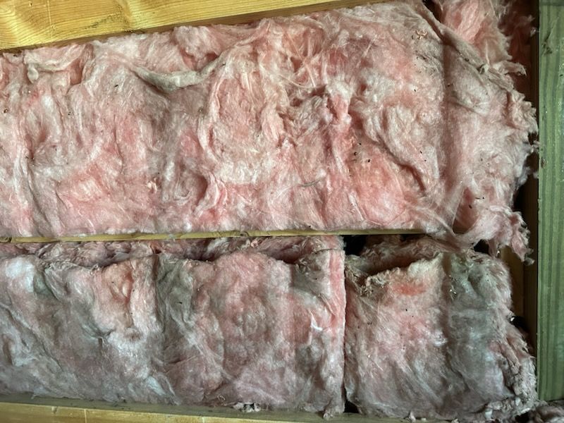 Pink fiberglass insulation batts stacked in a wooden frame, with foil or plastic backing visible.