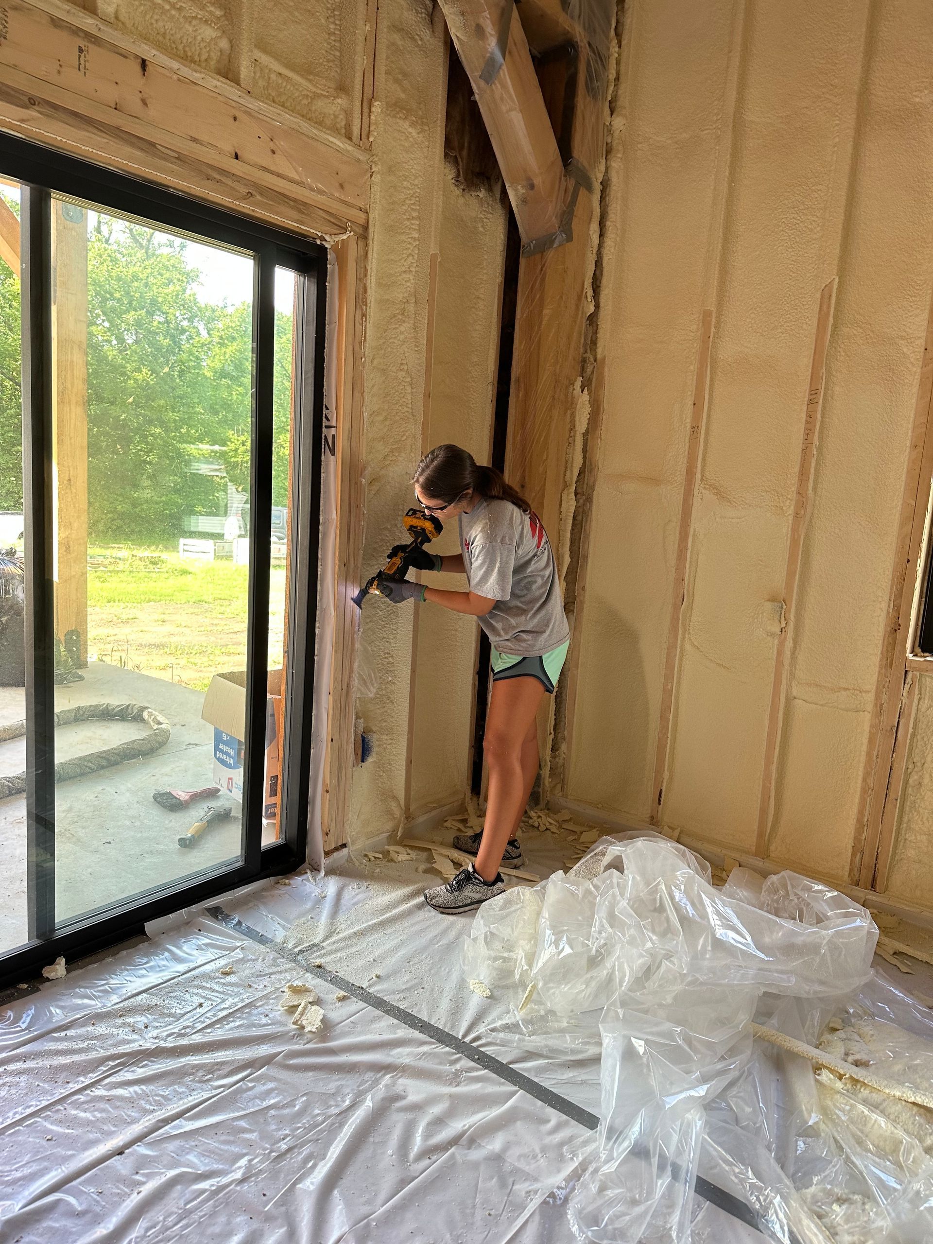 Person painting an unfinished interior wall near a glass door, with plastic sheeting on the floor.