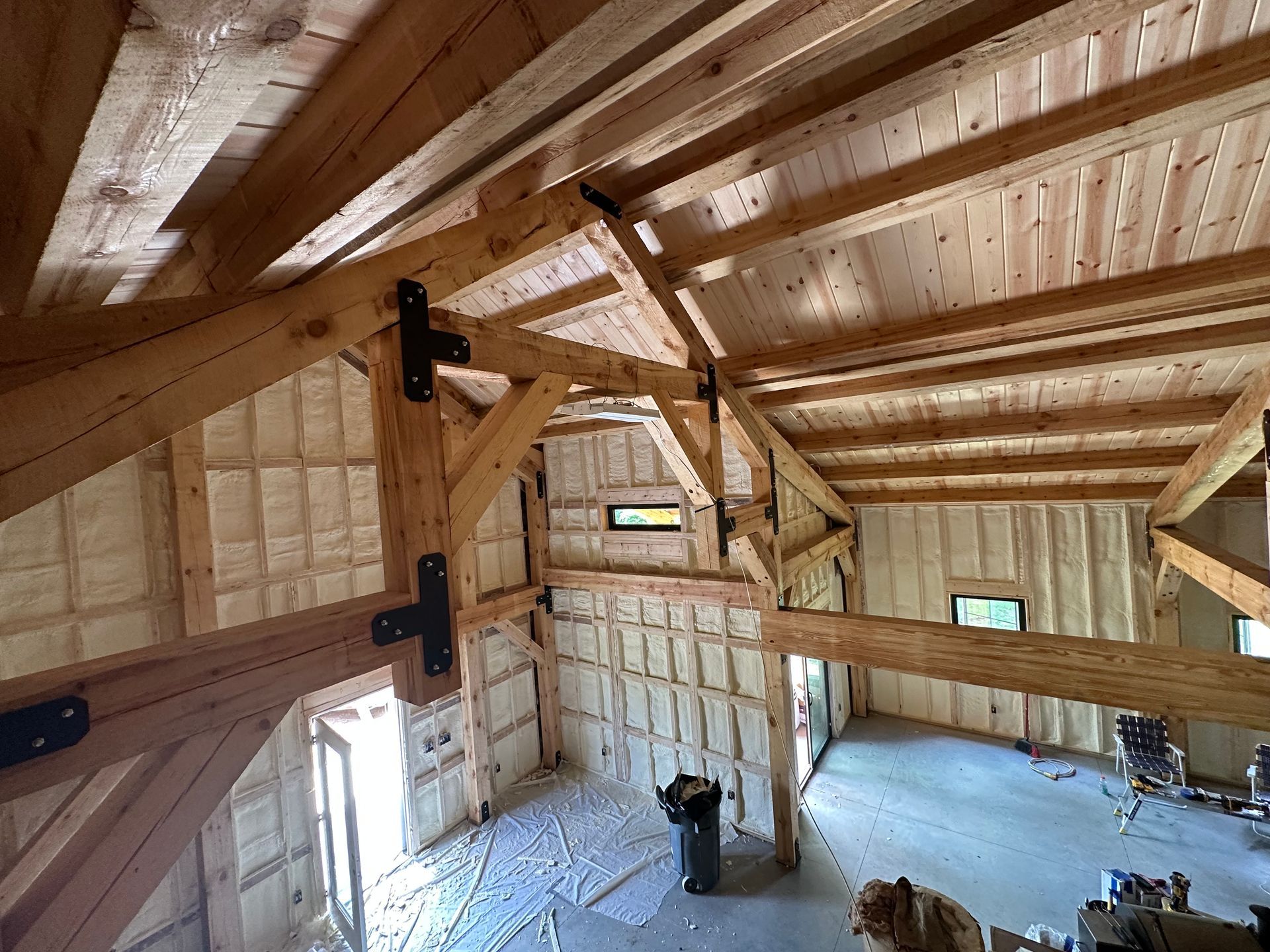 Interior of a wooden loft with exposed beams, wall panels, and small windows under a sloped roof.