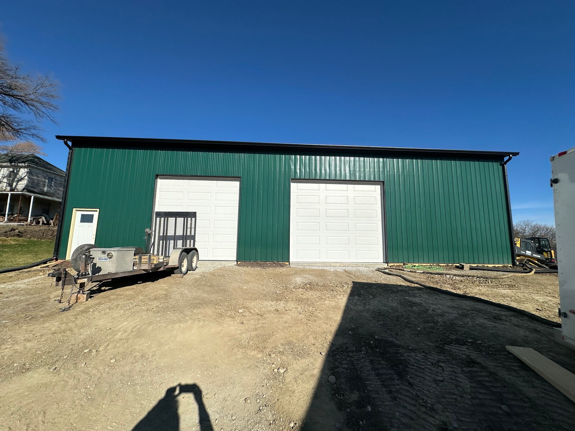 Green metal warehouse with two white roll-up doors on a dirt lot under a blue sky