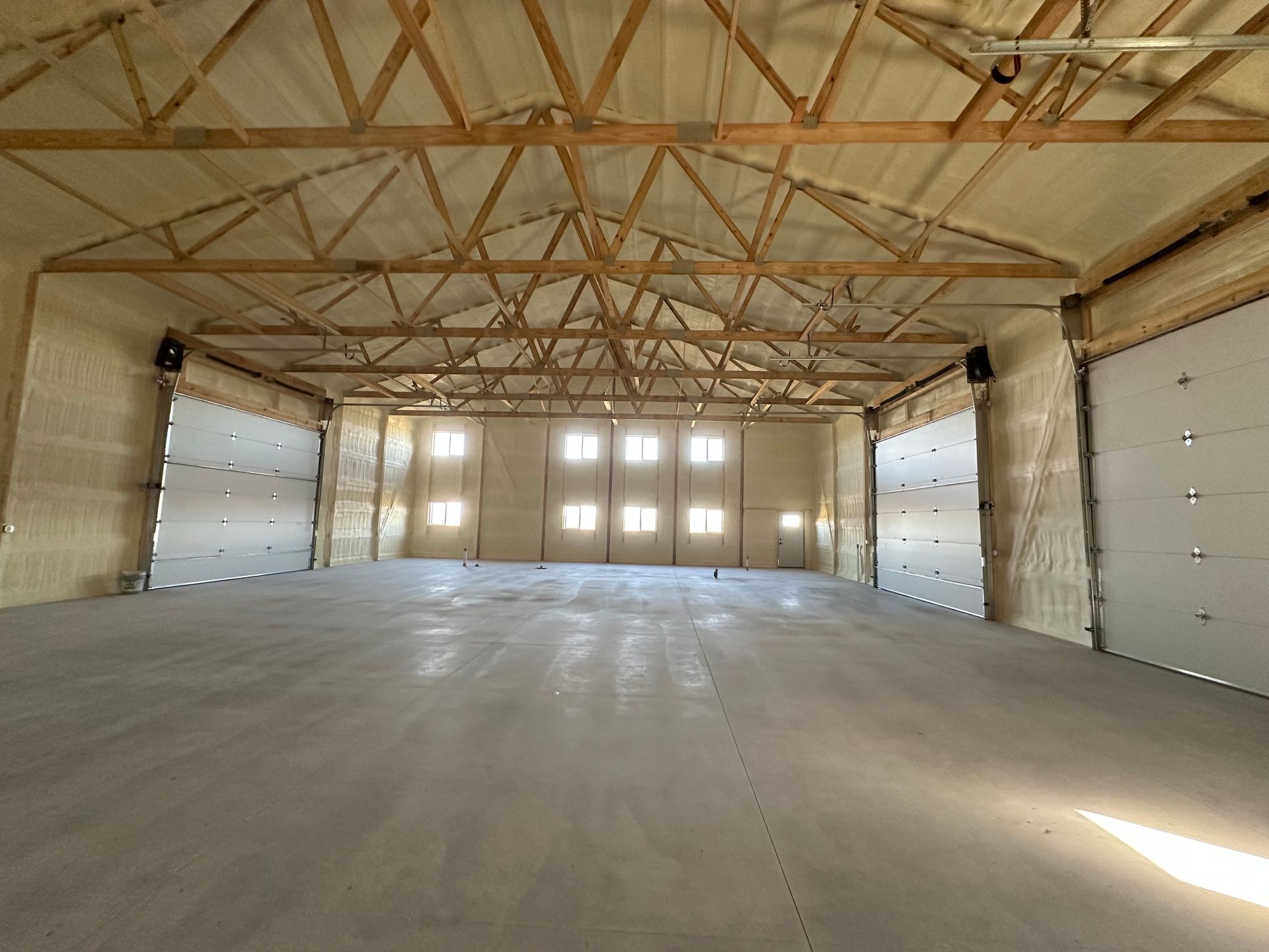 Empty wooden warehouse interior with exposed trusses, concrete floor, and large garage doors