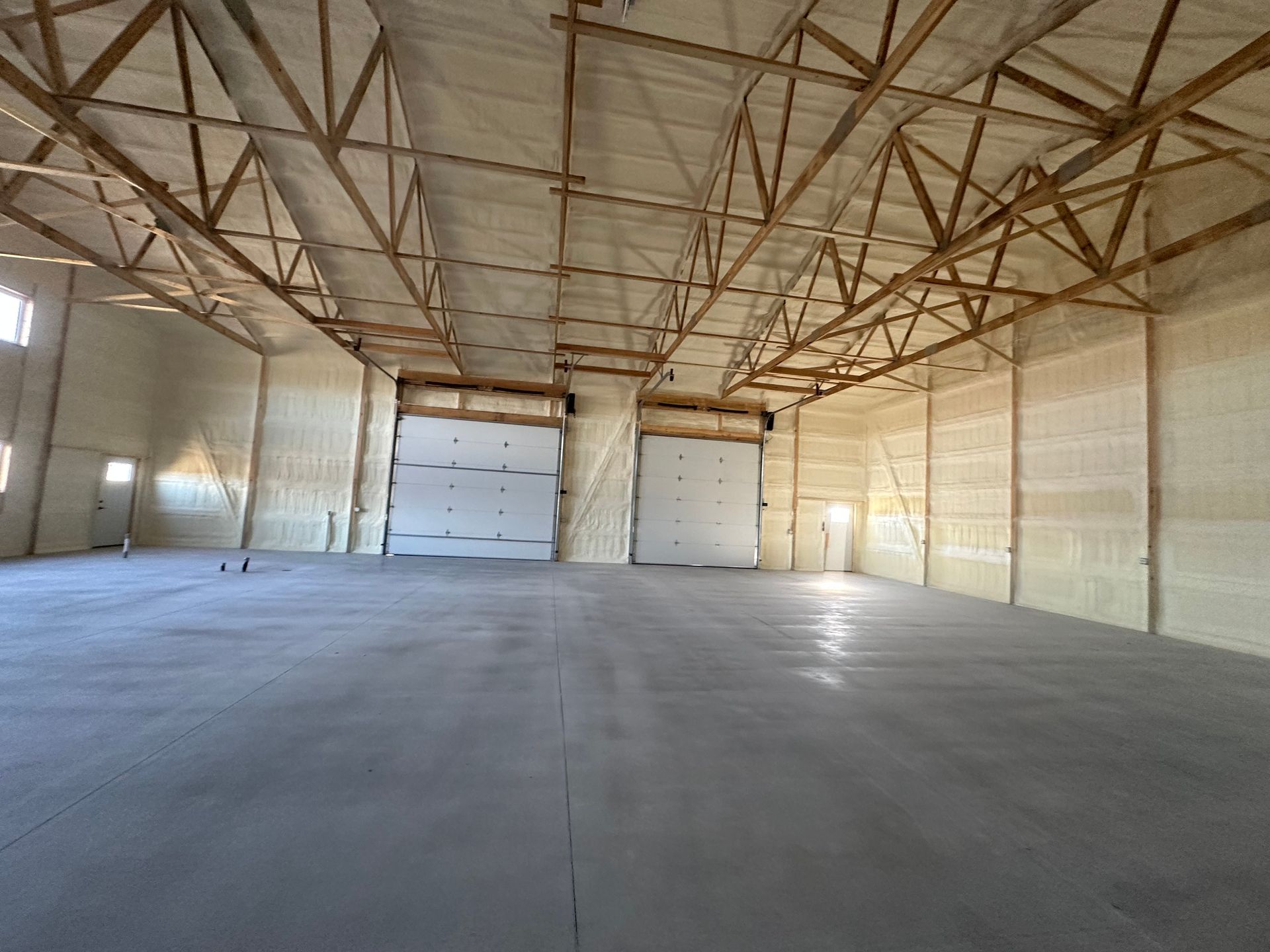 Empty warehouse interior with concrete floor, high truss ceiling, and large closed doors at the far end