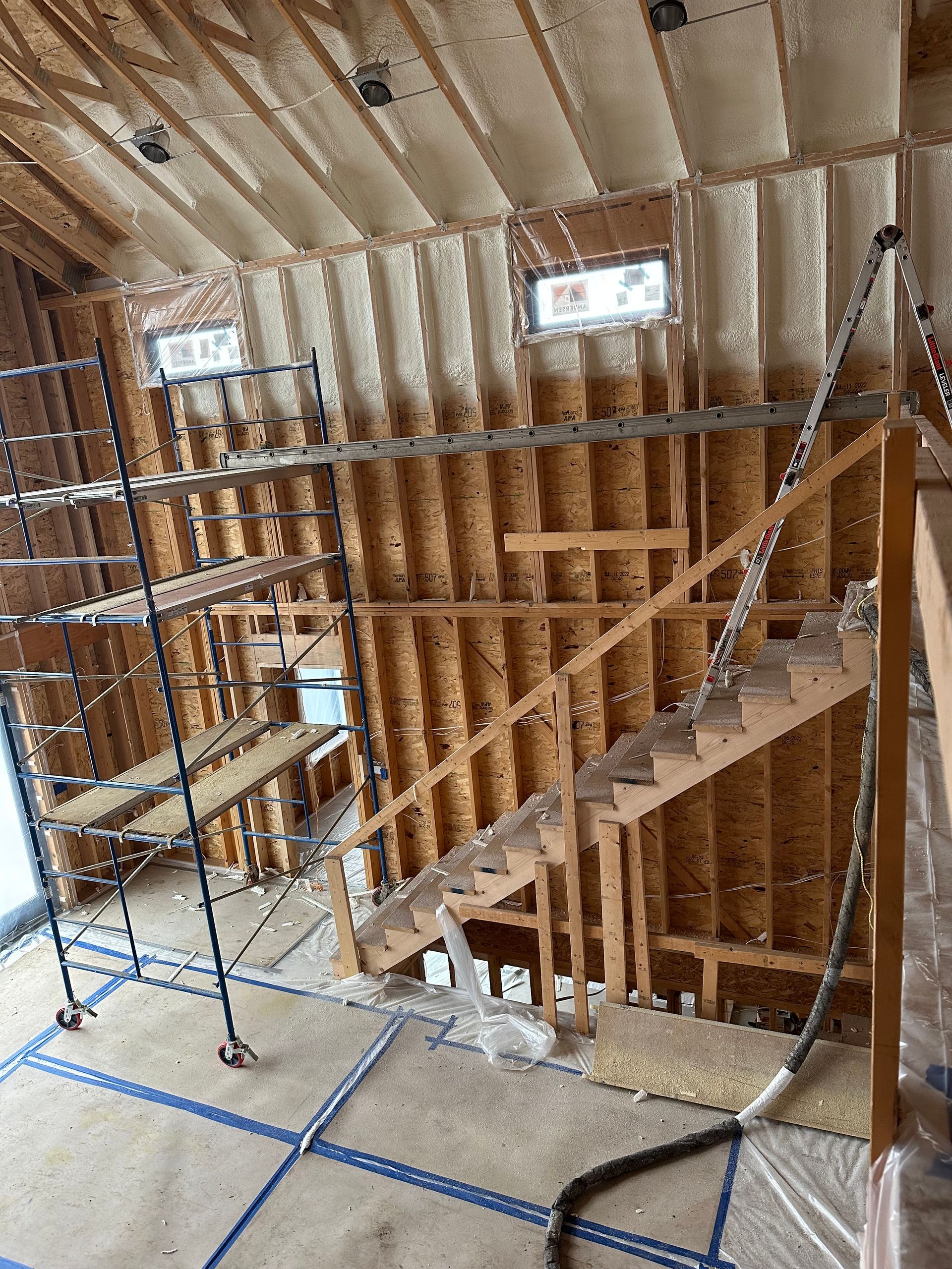 Interior construction site with wooden stair framing, metal scaffolding, and exposed insulation on the walls and ceiling