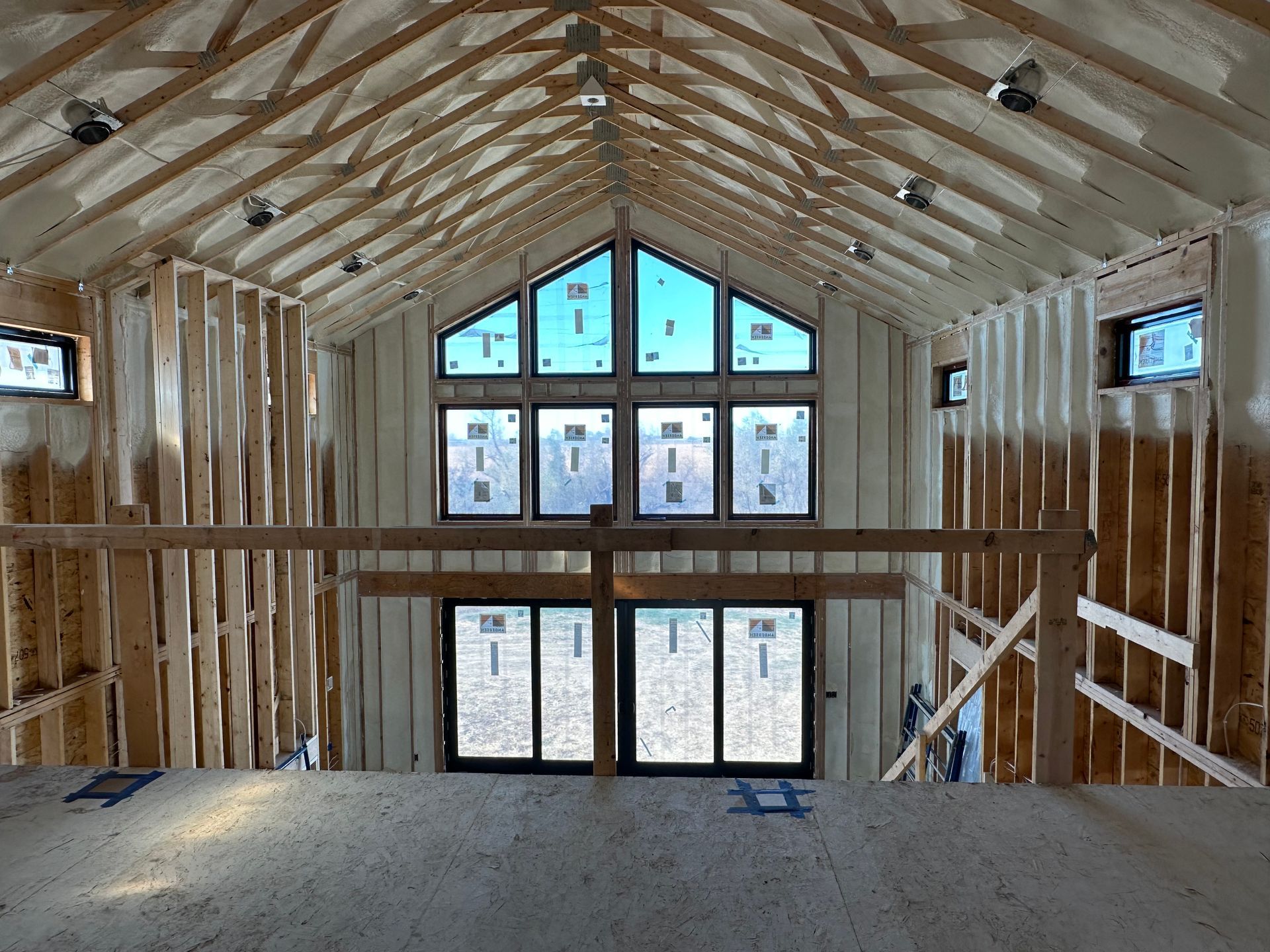 Interior of a framed house under construction with exposed wood trusses and large windows on both ends.