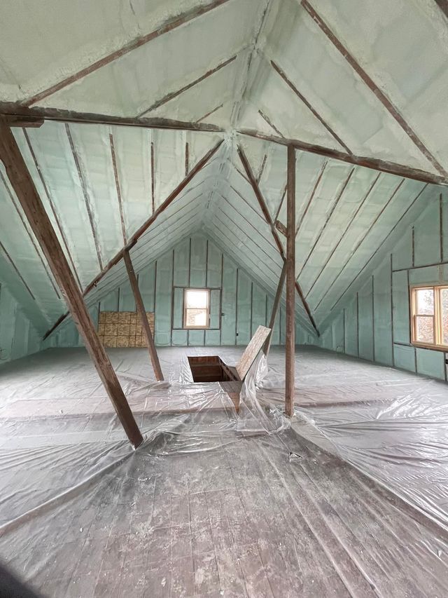Empty attic room with sloped mint-green walls, exposed beams, and two small windows