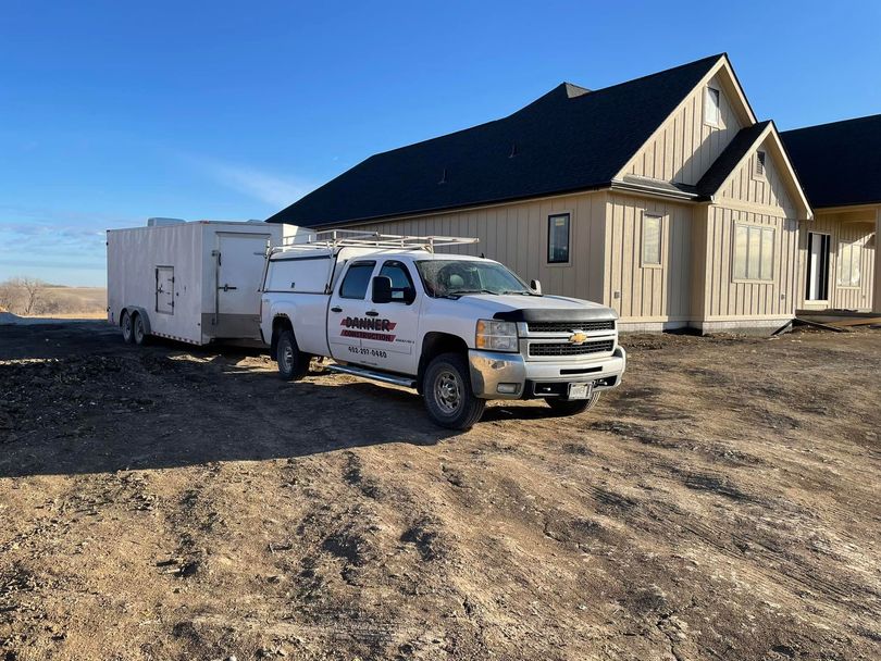 White utility truck parked beside a beige house on a dirt lot under a clear blue sky.