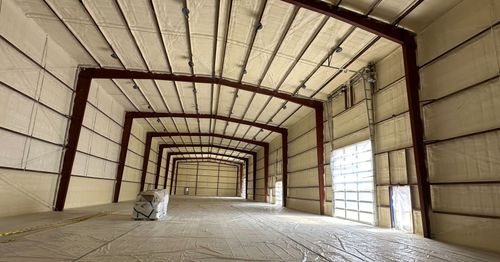 Empty industrial warehouse interior with metal frame walls, high ceiling, and concrete floor