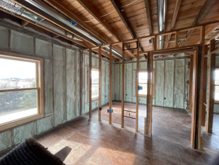 Unfinished room with exposed wood framing, insulation, and two windows, viewed from a corner.