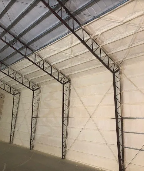 Interior of a large warehouse with metal support beams and white insulated walls and ceiling.
