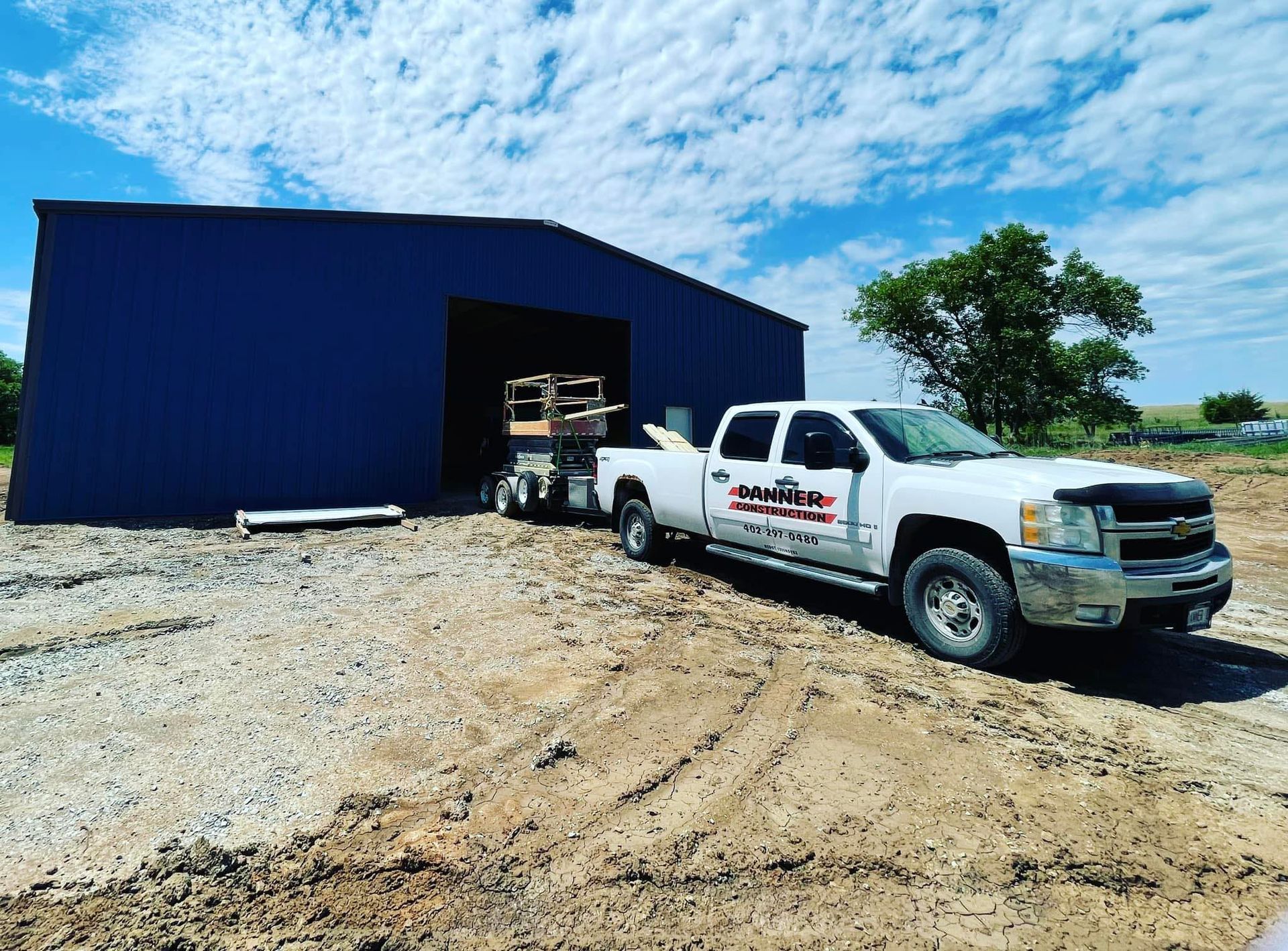 White pickup truck beside a blue metal building on a gravel lot under a bright sky