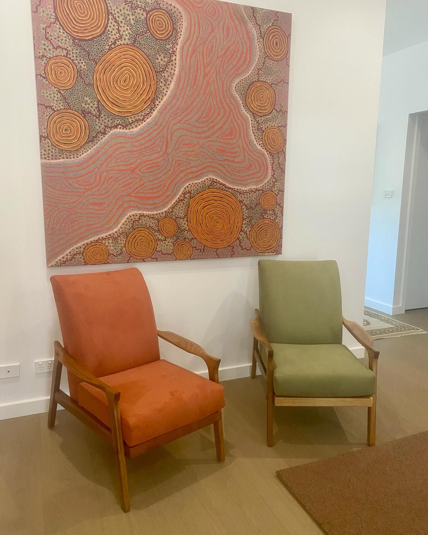 Two mid-century modern armchairs, orange and green, under a large abstract painting on a white wall - Metreson Upholstery, NSW.